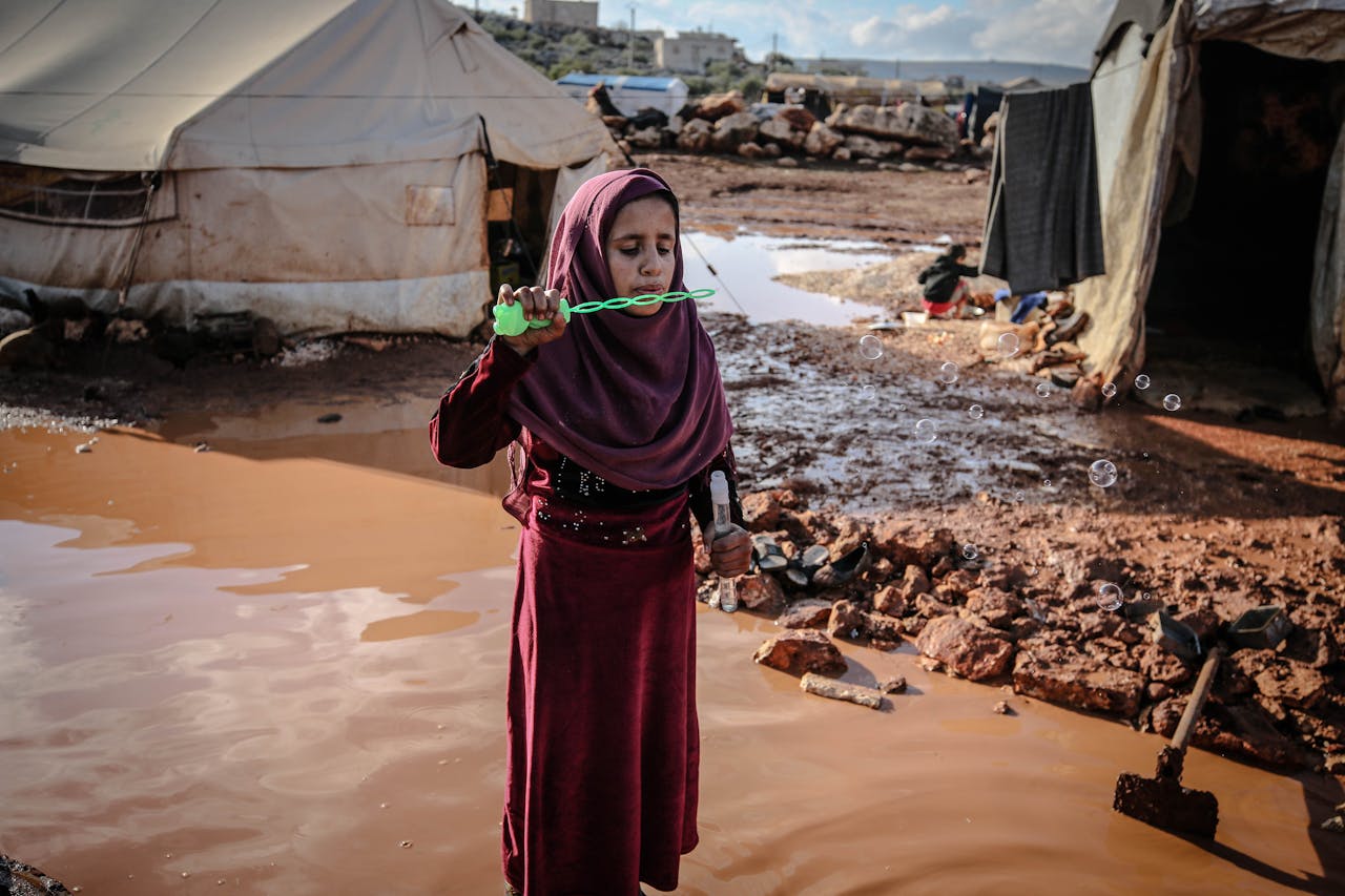 services-02 A young girl in Idlib refugee camp blowing bubbles, symbolizing innocence amidst adversity.