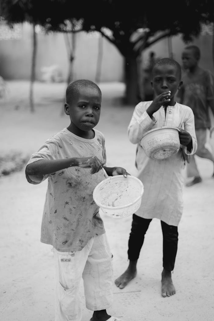 services-04 Black and white portrait of children holding bowls outdoors, evoking themes of poverty and hope.