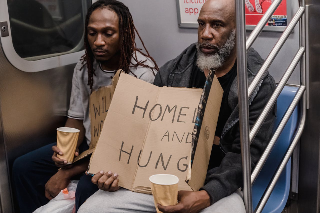 heros-img Two men holding signs about homelessness in a subway train emphasize urban hardship.